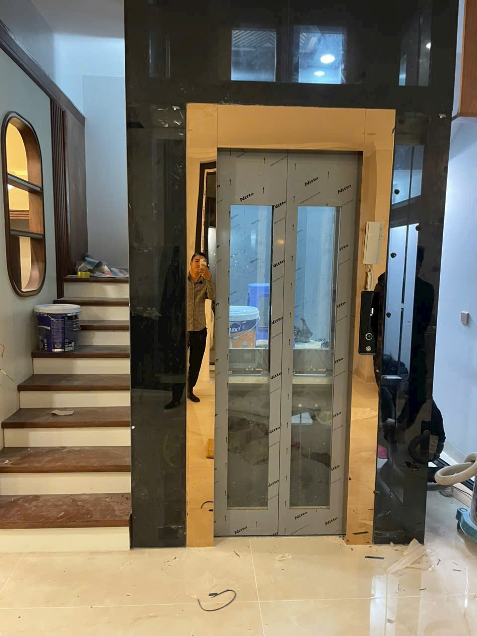 Thang máy gia đình cửa kính khung nhôm xám lắp cạnh cầu thang trong nhà đang hoàn thiện